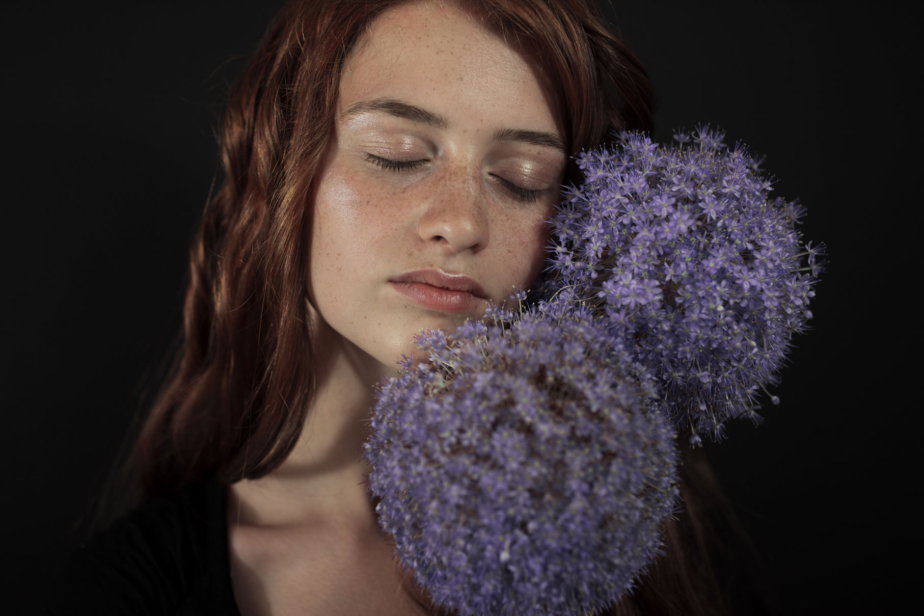 Jeune fille les yeux fermés avec des fleurs violettes.