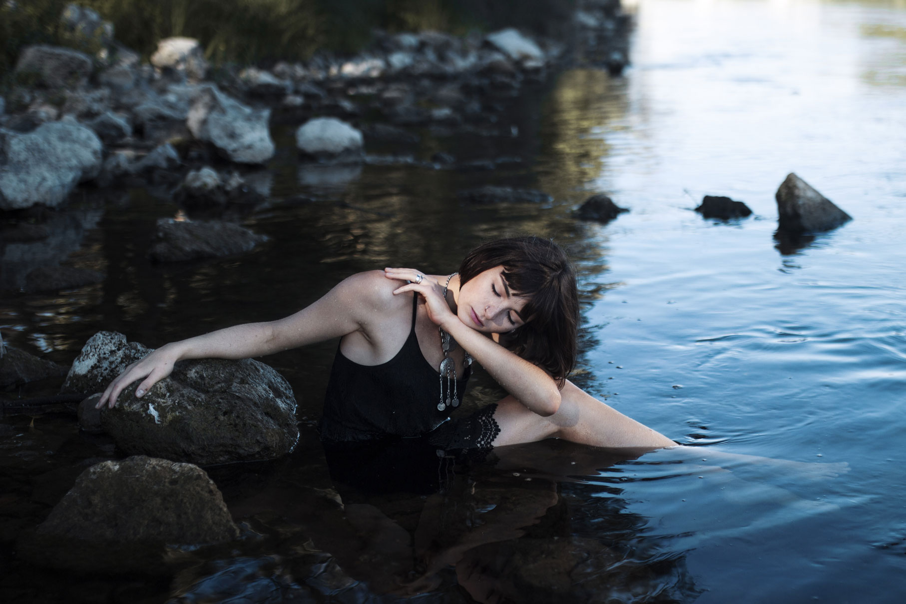 Jeune femme aux cheveux au carré dans l'eau d'un fleuve avec des rochers